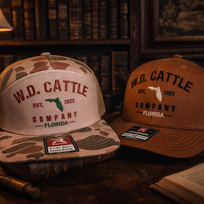 Two W.D. Cattle Company hats on a wooden surface with a lamp and books in the background.