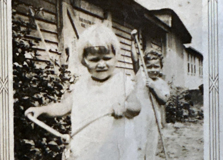 A little girl riding a tricycle in an old Polaroid photograph with the text "Gran" written in black pen. A little boy holds a stick behind the girl. 