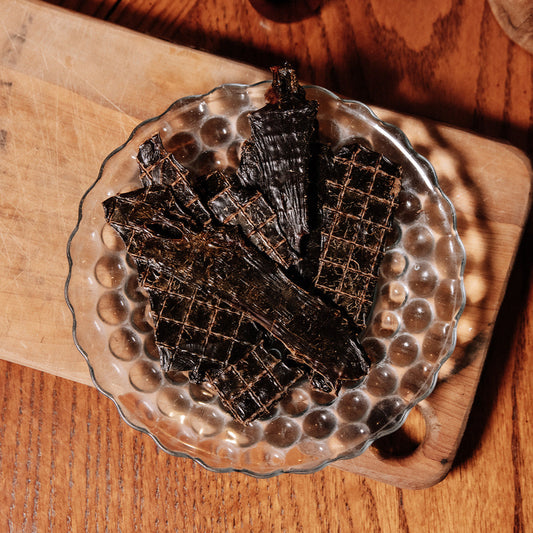Dark brown, dehydrated liver wafers lie on a glass plate with a wooden background and photographed from directly above. 