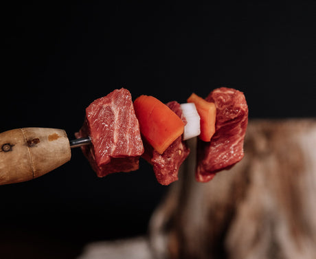Skewer with raw stew meat, orange bell pepper, and onions over a blurred background. 
