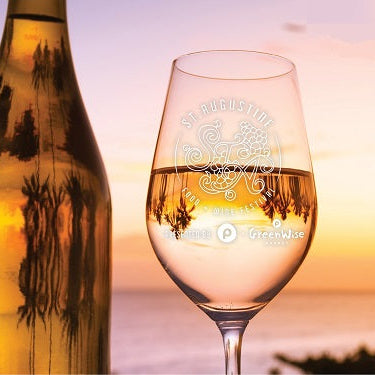 Wine bottle and glass with sunset and palm trees in the background. Text on the wine glass says "St Augustine, Food Wine Festival" and the Publix logo on the bottom of the glass next to Greenwise text and a unknown text to the left of the publix logo. 