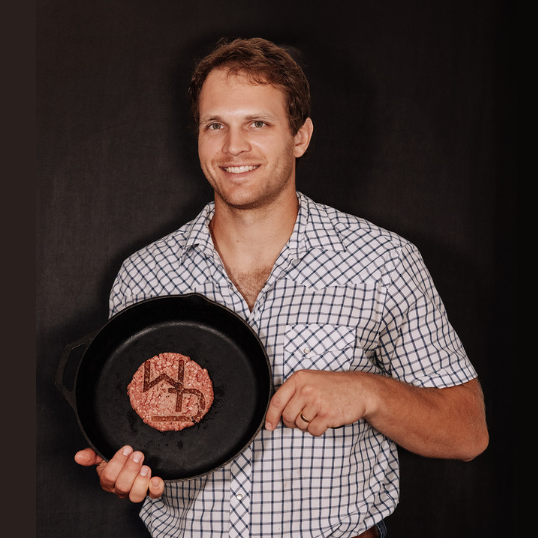 Tyler holding a skillet with a burger patty on it