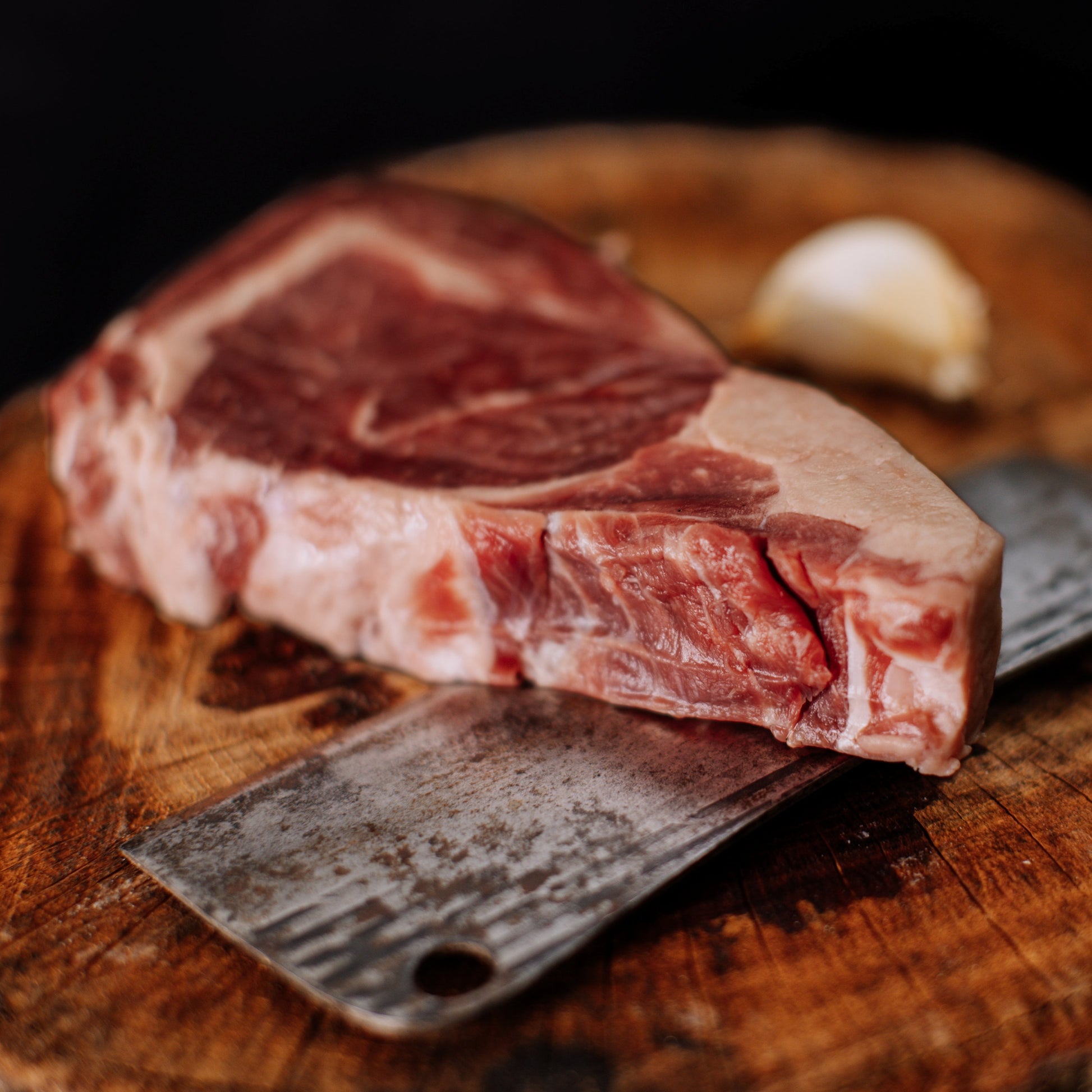 Deep red ribeye lying on its side on top of a cleaver, intended to showcase the ribeye thickness and marbling to the customer. 